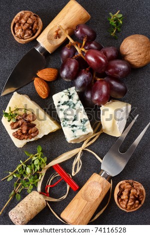 Three cheeses, almonds, walnut and grapes on a black background.