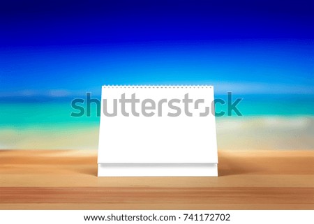 Blank desk calendar on wooden desk. Summer, beach, front view. Mockup template to replace your design.