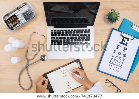 Doctor working at desk table with stethoscope and notebook with a visual test chart