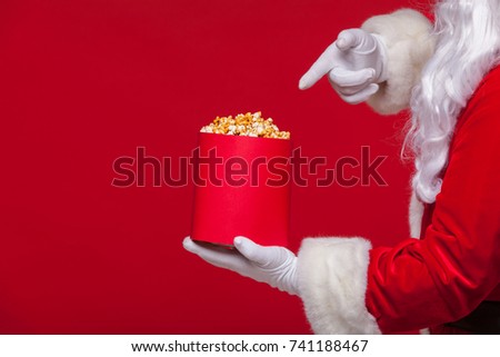 Christmas. Photo of Santa Claus gloved hand With a red bucket with popcorn, on a red background