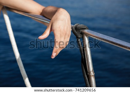 hand on the railing of a yacht against the background of sea water on a sunny day