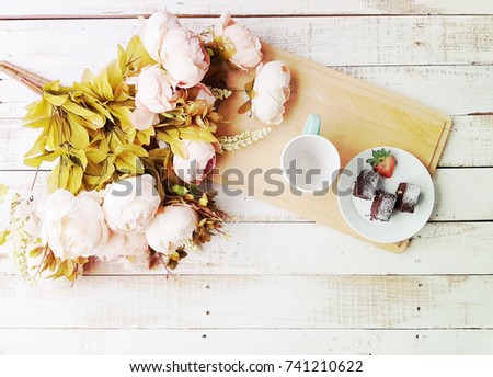 chocolate brownie with strawberry on dish and empty cup on woodboard with blossom flower on the white wood table and copyspace