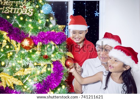 Picture of two grandchildren decorating a Christmas tree with their grandfather. shot at home