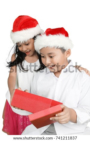 Portrait of two cute children open christmas presents box with impressed expression and wearing Santa hat, isolated on white background