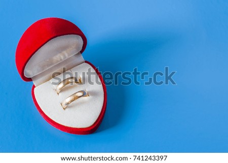 Gold wedding rings in a box of hearts. Blue background
