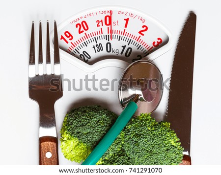 Diet healthy eating weight control and health care concept. Closeup green broccoli with stethoscope knife fork on white scales