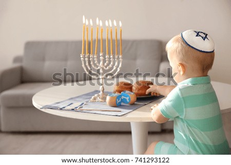 Cute boy sitting near nine-branched menorah on table at home