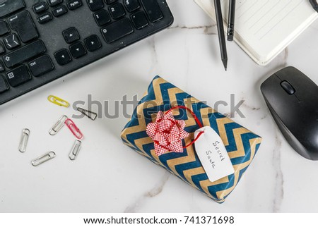 Office Christmas celebration concept, the idea of sharing gifts secret Santa. Keyboard, mouse, notebook, pens, pencils, Christmas gift. White office table, copy space top view