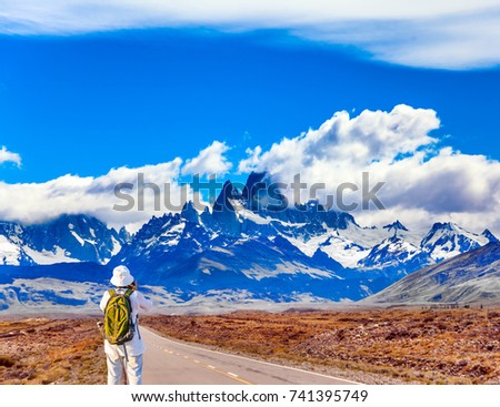 An elderly woman -  photographer with a backpack enthusiastically taking pictures of the highway to grandiose Mount Fitz Roy. The concept of active and ecological tourism
