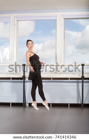 A pregnant woman dances ballet in class 