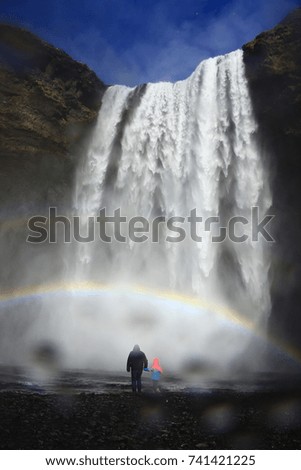  Dad and kid under the rainbow at the foot of Skogafoss heavy waterfall in Iceland