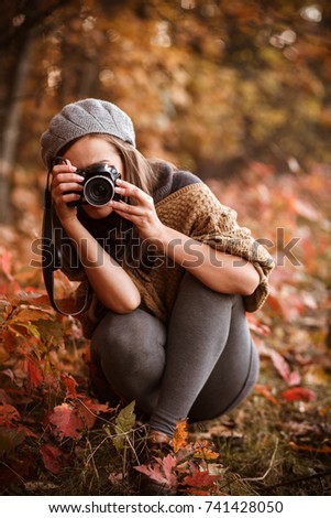 young woman taking pictures with photo camera in autumn forest