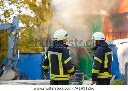 two firefighters stand back on a fire, on the background of the fire