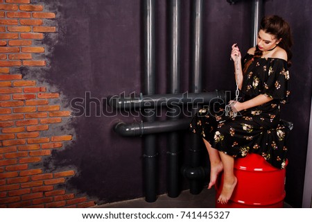 Black girl in dress with bright make-up and chain sitting on red barrel at studio. Halloween theme.