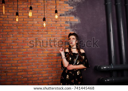 Black girl in dress with bright make-up and chain at hands posing at studio background brick wall. Halloween theme.