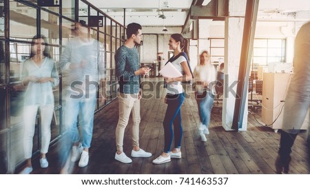 Young creative people in modern office. Successful hipster team in coworking. Businesspeople walking in the corridor of an business center. Motion blur. Couple of freelancers are discussing new ideas.