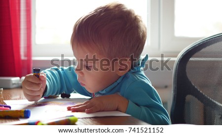 The child enthusiastically draws with crayons on a piece of paper. Preschool education
