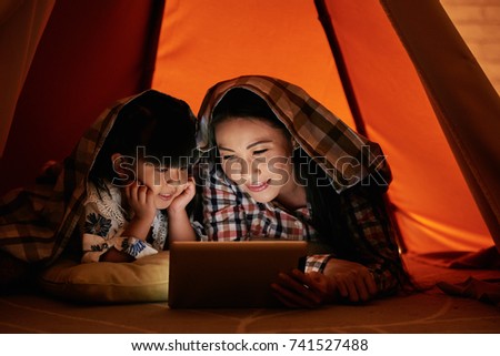 Little girl and her mother watching movies on digital tablet