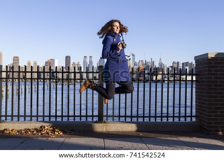 Young woman jumps with camera in front of Manhattan, at Edgewater.
