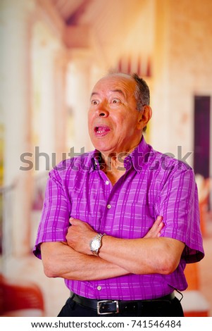 Portrait of a happy mature man, with his arms crossed and wearing a purple square t-shirt in a blurred background