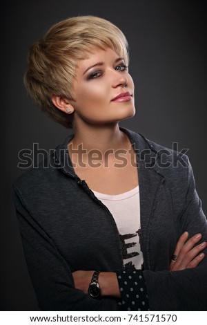 Happy smiling young business blond woman with short bob hair style looking in grey trendy jacket with fashion watch on the hand on dark background