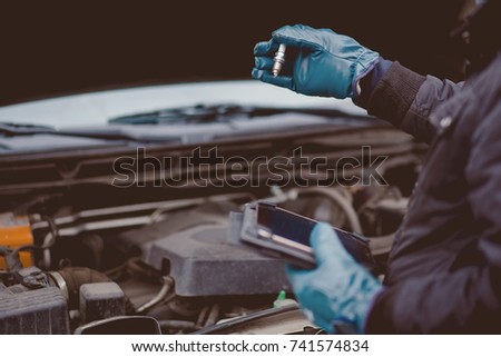 Automechanic conducts diagnostics of the spark plug machine using a tablet computer