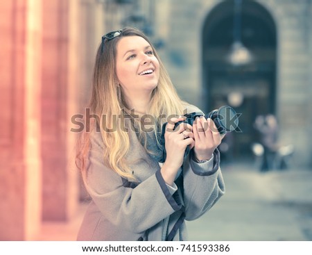 Young cheerful woman with a camera looking curious and taking a pictures outdoors