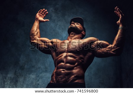 Young strong man bodybuilder in cap on wall background. Dark dramatic colors. Royalty-Free Stock Photo #741596800