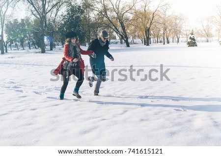 Couple running through the forest happy and joyful holding hands on romantic date in winter snow landscape.