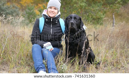 A girl is taking pictures with her dog, looking at the camera. Photo