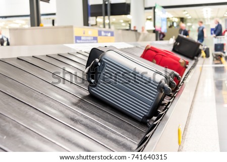 Suitcase on luggage conveyor belt at baggage claim at airport. Lines of people waiting for their baggage Royalty-Free Stock Photo #741640315