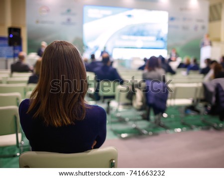 Business brunette woman with long hair and people Listening on The Conference or on the training in the hall,  woman looks thoughtfully at the presentation screen