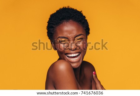 Cheerful young african woman with vivid makeup on her eyes. Female model laughing against yellow background.