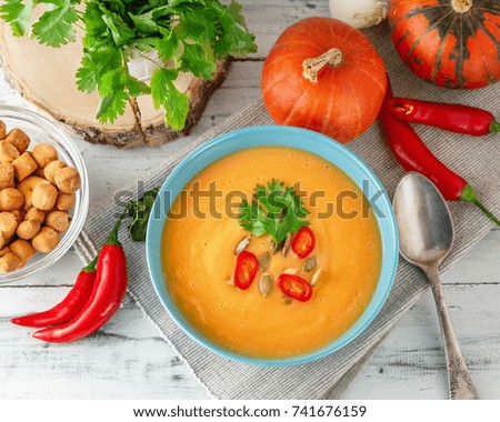 Pumpkin soup with chili pepper, pumpkin seeds, croutons and parsley in blue bowl on white wooden background