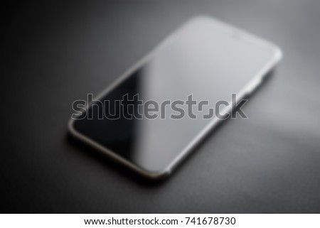 Modern mobile device like iPhone XS model.New smartphone blur background.Out of focus cellphone with big infinity edge display.Touchscreen panel on black background