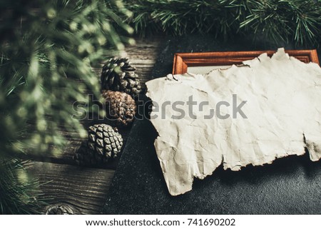 new year and Christmas composition on wooden table is a branch of tree, cones, photo frame and old yellow paper