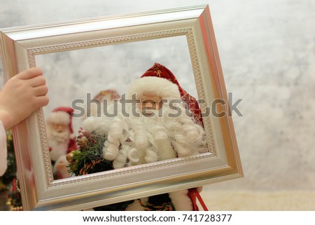 close up of a Santa ornament. Child hands holding a frame around Santa Claus. Father Christmas inside a golden frame with a winter background 