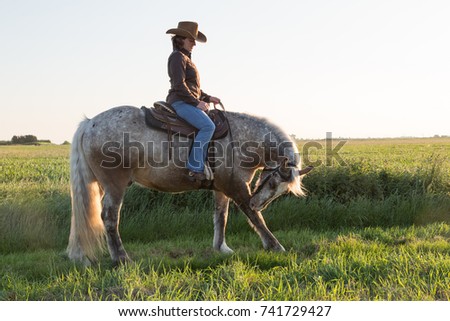 Young woman western cowgirl on horse. Low evening light sunset. Cowboy hat 