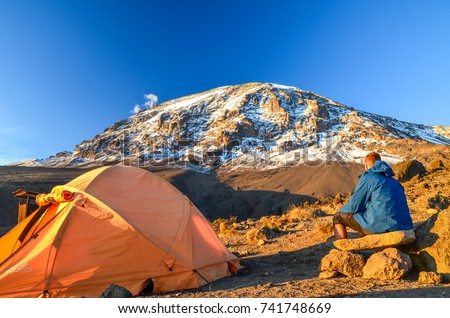 Evening view of Kibo with Uhuru Peak (5895m amsl, highest mountain in Africa) at Mount Kilimanjaro,Kilimanjaro National Park,seen from Karanga Camp at 3995m amsl. Tent and young hiker in foreground. Royalty-Free Stock Photo #741748669