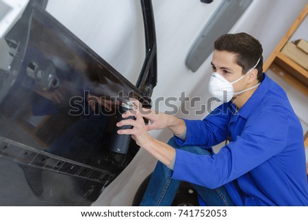 mechanic using a spray with paint for painting a car