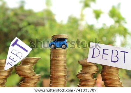 Miniature car carry coins on straight rolls of money among other unsafe rolls with "Debt" word write on white paper in natural