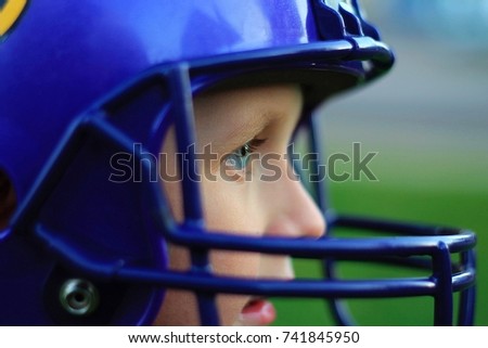a young Caucasian boy wearing a purple football helmet. Side view close up of face. blue eyes. Vikings helmet. 
