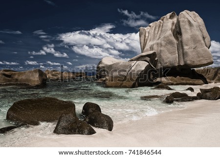 Rocks emerging from the sea in Anse Marron, La Digue, Seychelles pictured from the beach with blue sky and clouds