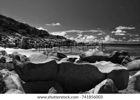 Rocks emerging from the sea in Anse Marron, La Digue, Seychelles pictured from the beach with blue sky and clouds