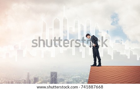 Young businessman standing on edge of house brick roof and looking down. Mixed media