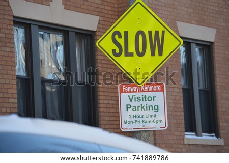 Slow bright diamond yellow street sign in the urban city landscape with a brick building wall with two windows