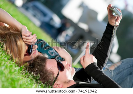 Young emotional happy teenage couple taking picture on grass in city park
