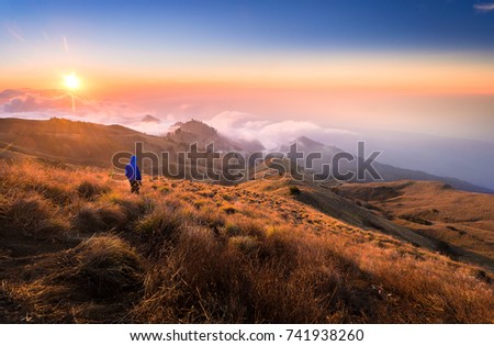 Hiker man with blue jacket standing, during dramatic gold sunset at Rinjani mountain, Lombok, Indonesia