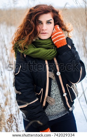 a young girl walks in the field. Dressed in winter clothes, she has blue eyes and thick red hair . Hair curls , the color of fire .