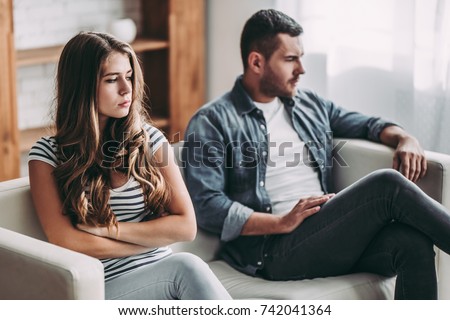 Upset couple at home. Handsome man and beautiful young woman are having quarrel. Sitting on sofa together. Family problems. Royalty-Free Stock Photo #742041364